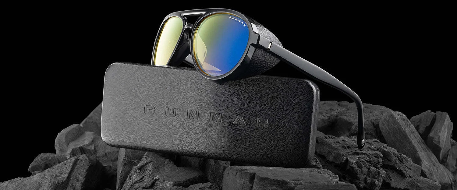 Gunnar Tallac Computer Glasses, featuring a black premium acetate frame and reflective lenses, are elegantly displayed on a GUNNAR case against dark textured rocks.