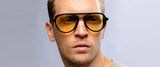 A man wears Gunnar Tallac Computer Glasses by Gunnar with oversized mountaineer-style, yellow-tinted lenses for blue light filtering. With a neutral gaze to the side, the premium acetate frame offers understated elegance.