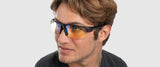 A man wears Gunnar Torpedo 360 Computer Glasses, featuring tinted, interchangeable lenses, and gazes thoughtfully to the side against a plain background.