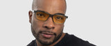 A man, in Gunnar Vertex Computer Glasses with blue light protection and a black shirt, gazes at the camera against a light gray backdrop.