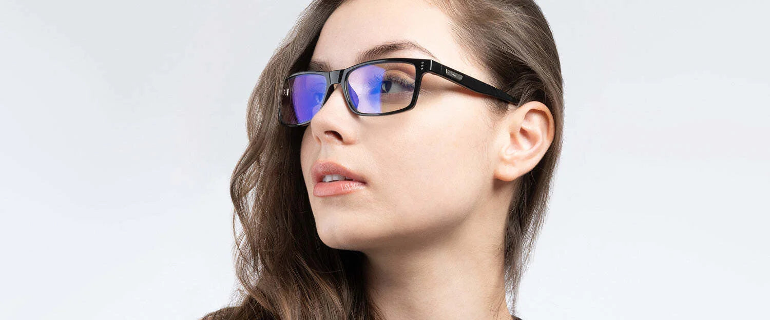 A person with long hair wears Gunnar Vertex Computer Glasses, size 55, featuring blue-tinted lenses for blue light protection, and looks to the side against a gray background.