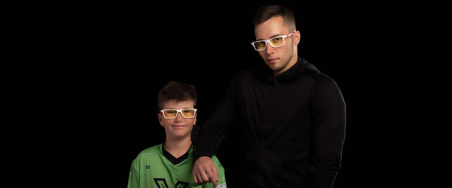 Two individuals, one in a green shirt and the other in black, wear Gunnar Vertex Collection for St Jude Computer Glasses against a black background. These stylish frames feature patented Gunnar lens technology for optimal eye protection and comfort.