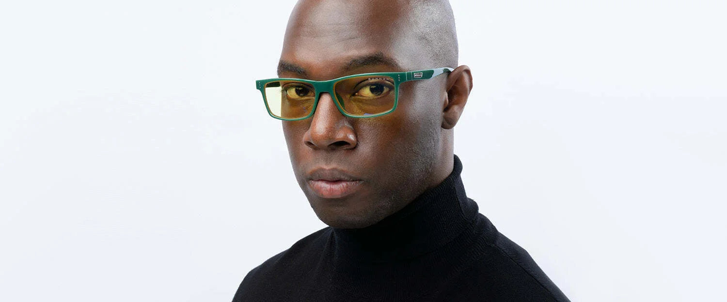 A person in a black turtleneck is wearing Gunnar Vertex Computer Glasses with stylish green rectangular lenses and a durable nylon frame, set against a white background.