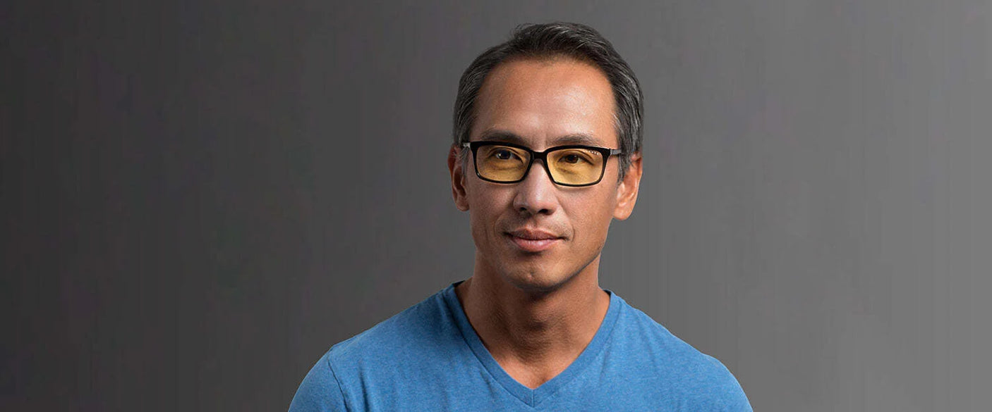 A man with short hair, wearing Gunnar Vertex Computer Reading Glasses in Size 55 and a blue V-neck shirt, looks straight at the camera against a gray background.