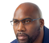 A man with a beard, wearing John Raymond BREAK Eyeglasses in size 60 and a blue shirt, gazes thoughtfully to the side against a white background.