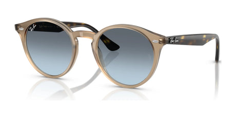 The Ray-Ban RB2180F Sunglasses feature brown frames and blue gradient lenses, stylishly reflecting light on a white surface and providing classic UV protection.