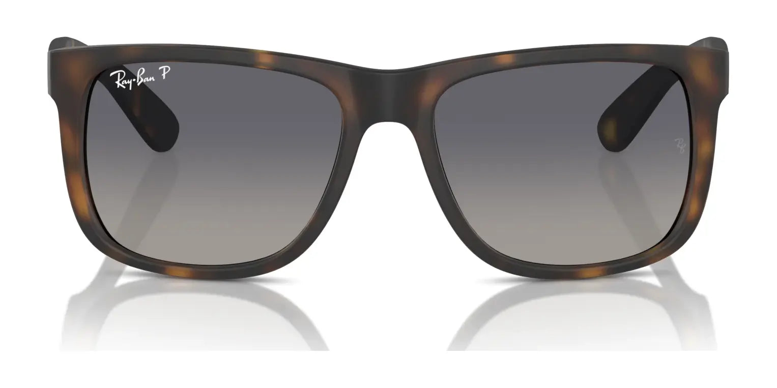 The Ray-Ban JUSTIN RB4165 Sunglasses, with their tortoise-shell pattern and dark gradient lenses, elegantly rest on a reflective surface. They provide 100% UV protection for a stylish yet practical eyewear choice.