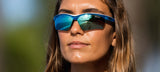 Sporting Tifosi Optics VERO Sunglasses, ideal for smaller faces, a long-haired individual delights in beachy vibes through the reflective blue lenses, perfect for action-packed days.