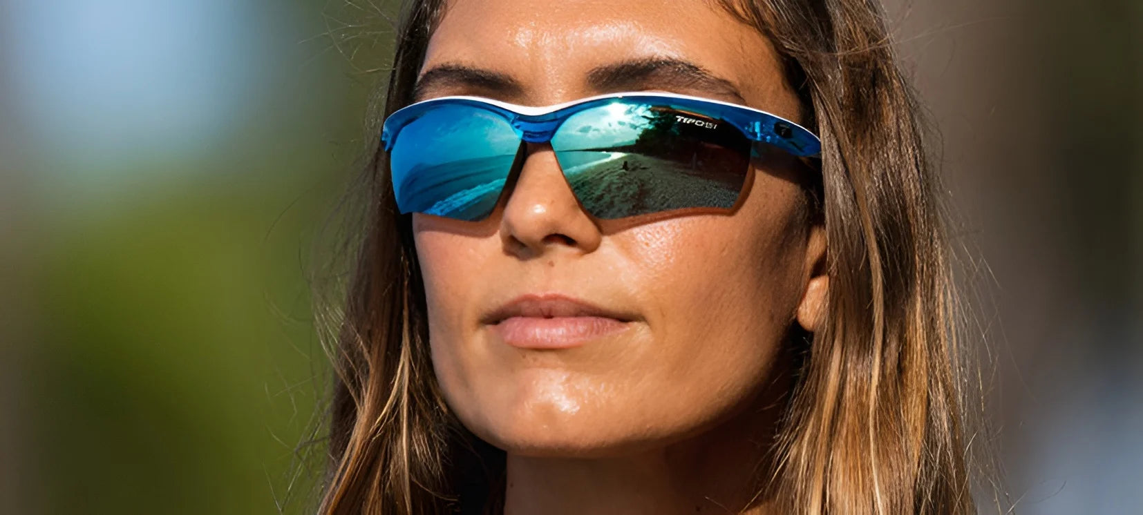 Sporting Tifosi Optics VERO Sunglasses, ideal for smaller faces, a long-haired individual delights in beachy vibes through the reflective blue lenses, perfect for action-packed days.