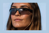 Person with long hair wearing Tifosi Optics VERO Sunglasses, size 64, looking into the distance against a clear blue sky.