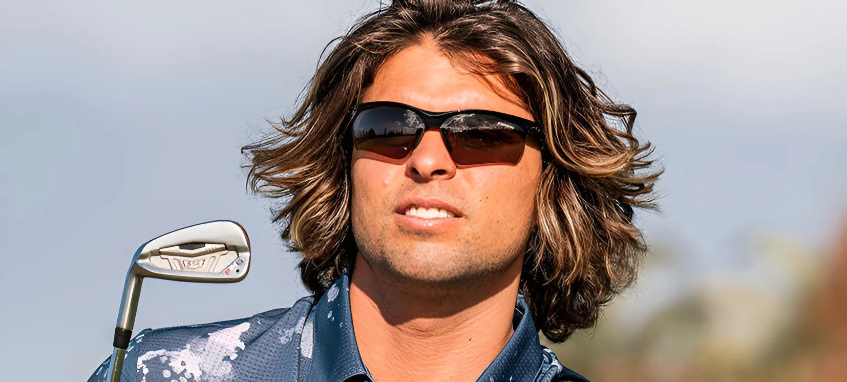 Someone with long hair is outdoors, holding a golf club and wearing Tifosi Optics VERO Sunglasses, perfect for multi-sport activities and suited for smaller faces.