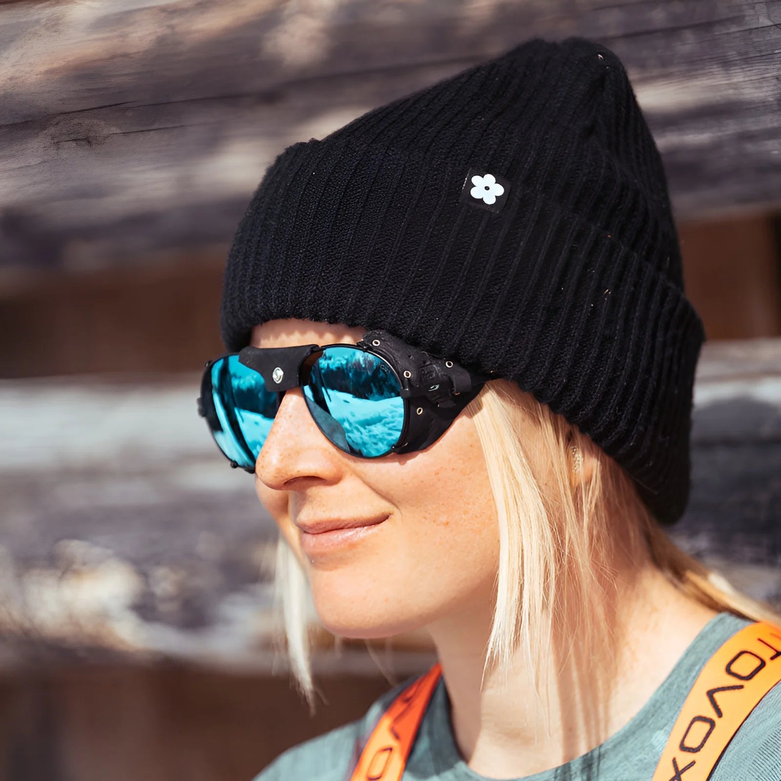 A person outdoors is smiling while wearing a black beanie and gray top with orange straps, sporting reflective Julbo Cham Sunglasses, Size 58.