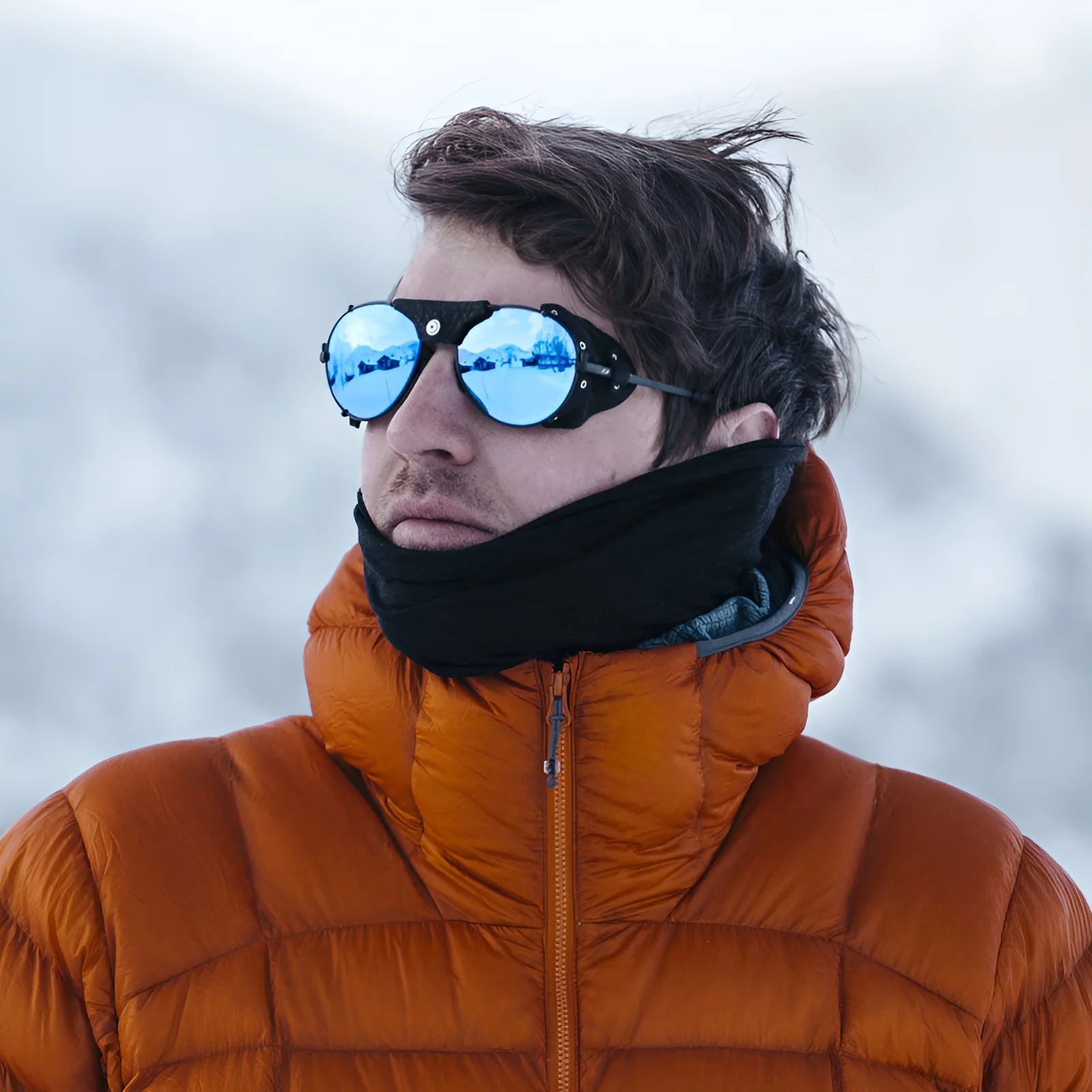 A person wearing a black scarf and Julbo Cham sunglasses against a snowy backdrop.