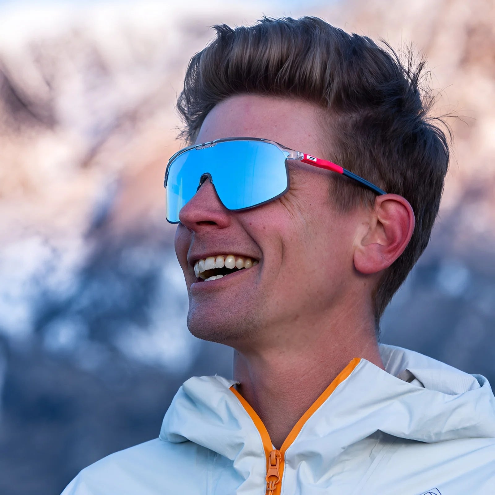 A person enjoying the outdoors with a mountain backdrop wears Julbo Density Sunglasses and a white jacket, blending style and functionality.