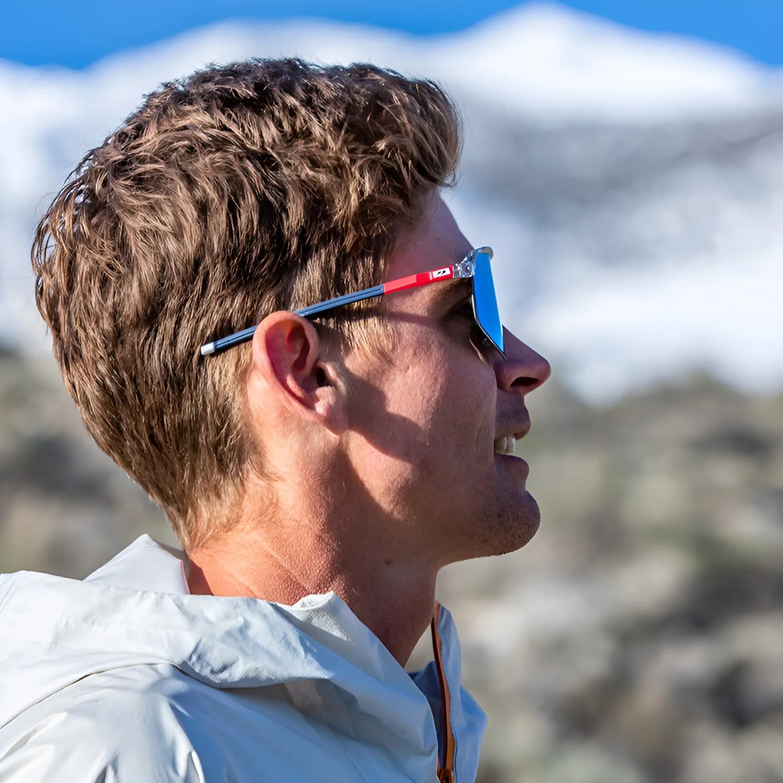 Wearing Julbo Density Sunglasses with CustomFit Temples for a snug fit, a person gazes at snowy mountains in the background.