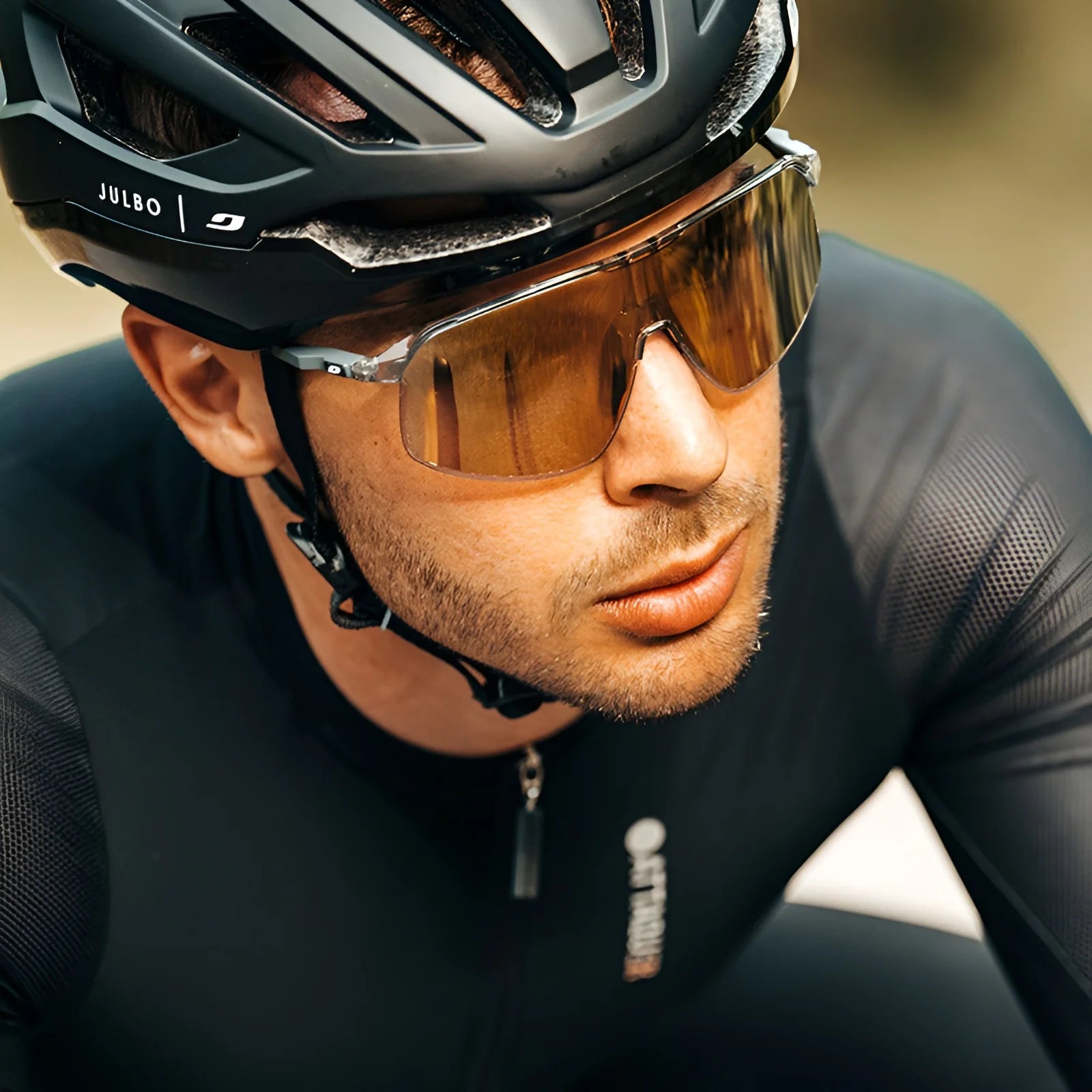 A cyclist wearing a helmet and the black Julbo Density Sunglasses with CustomFit Temples for comfort is focused ahead. The sleek Julbo design provides optimal ventilation during movement.