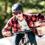 A person in a red plaid shirt and helmet rides a bike outdoors under the sun, enjoying the wide field of vision offered by Julbo Fury S Sunglasses with Spectron lenses.