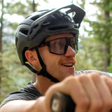 Wearing Julbo Fury sunglasses and a bike helmet, the person confidently grips the handlebars. With trees blurred in the background, their REACTIV photochromic lenses adapt effortlessly to changing light conditions.