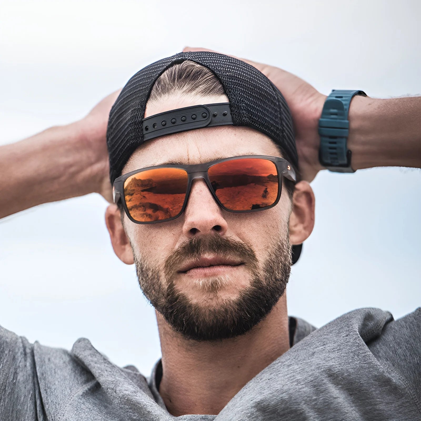 A bearded man wears Julbo Renegade Sunglasses with REACTIV photochromic lenses and Grip Tech Temples. Hands on head, sunglasses backward on his cap, he confidently gazes at the camera.