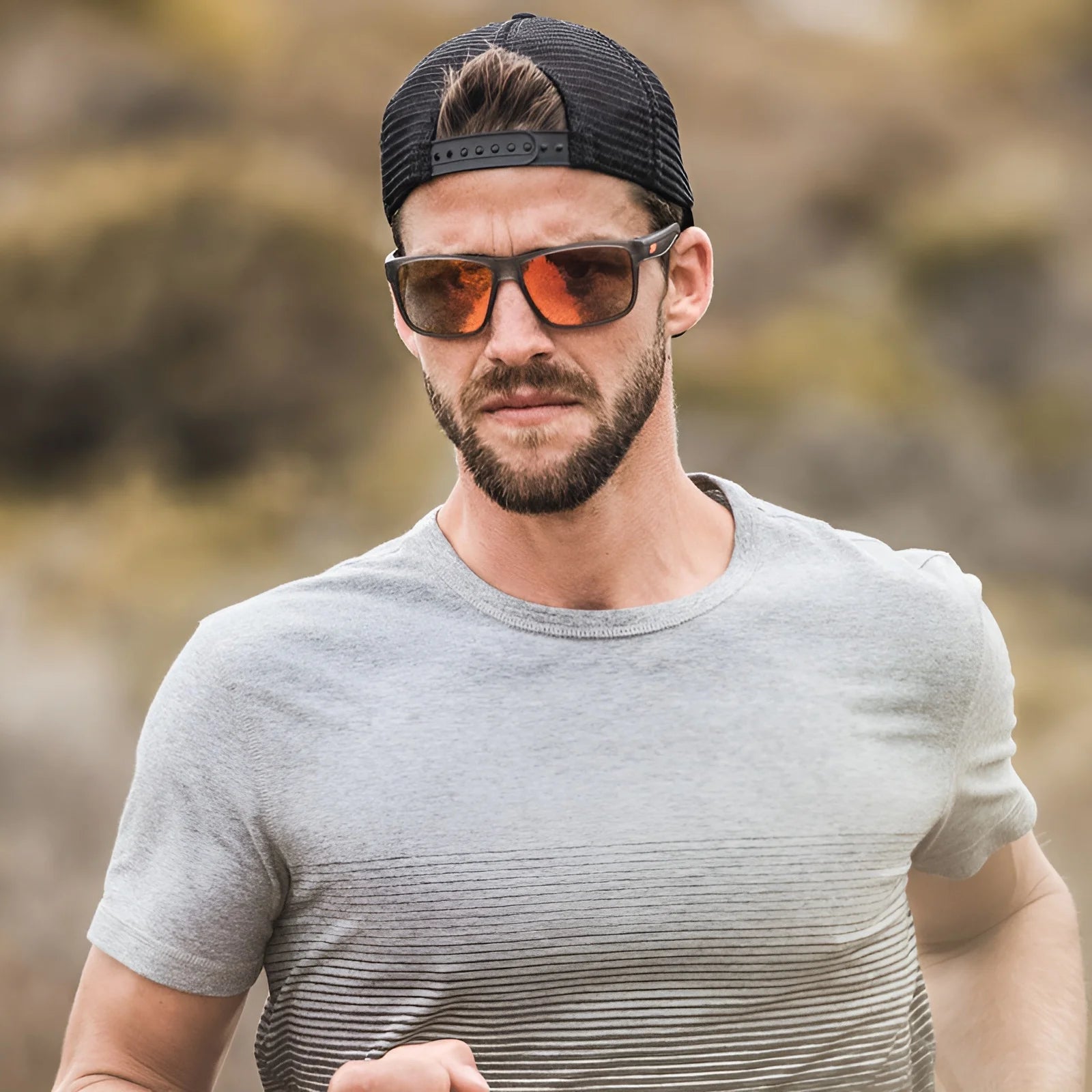 A man races through nature with Julbo Renegade Sunglasses, Size 61, confidently on his nose. A black cap rests atop his head, and a gray T-shirt hugs his athletic frame. Thanks to Grip Tech Temples from Julbo, those shades stay secure as he tackles any challenge.