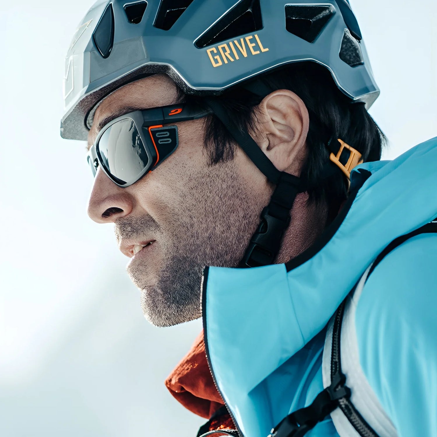 A person in a blue jacket and helmet, wearing Julbo Shield Sunglasses featuring Grip Nose technology, looks ahead outdoors.