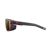 The Julbo Shield Sunglasses, size 59, showcase a sleek profile with black sports design, red accents, and side shields. Equipped with Grip Nose technology for a secure fit and Air Flow ventilation for optimal comfort during intense activities.