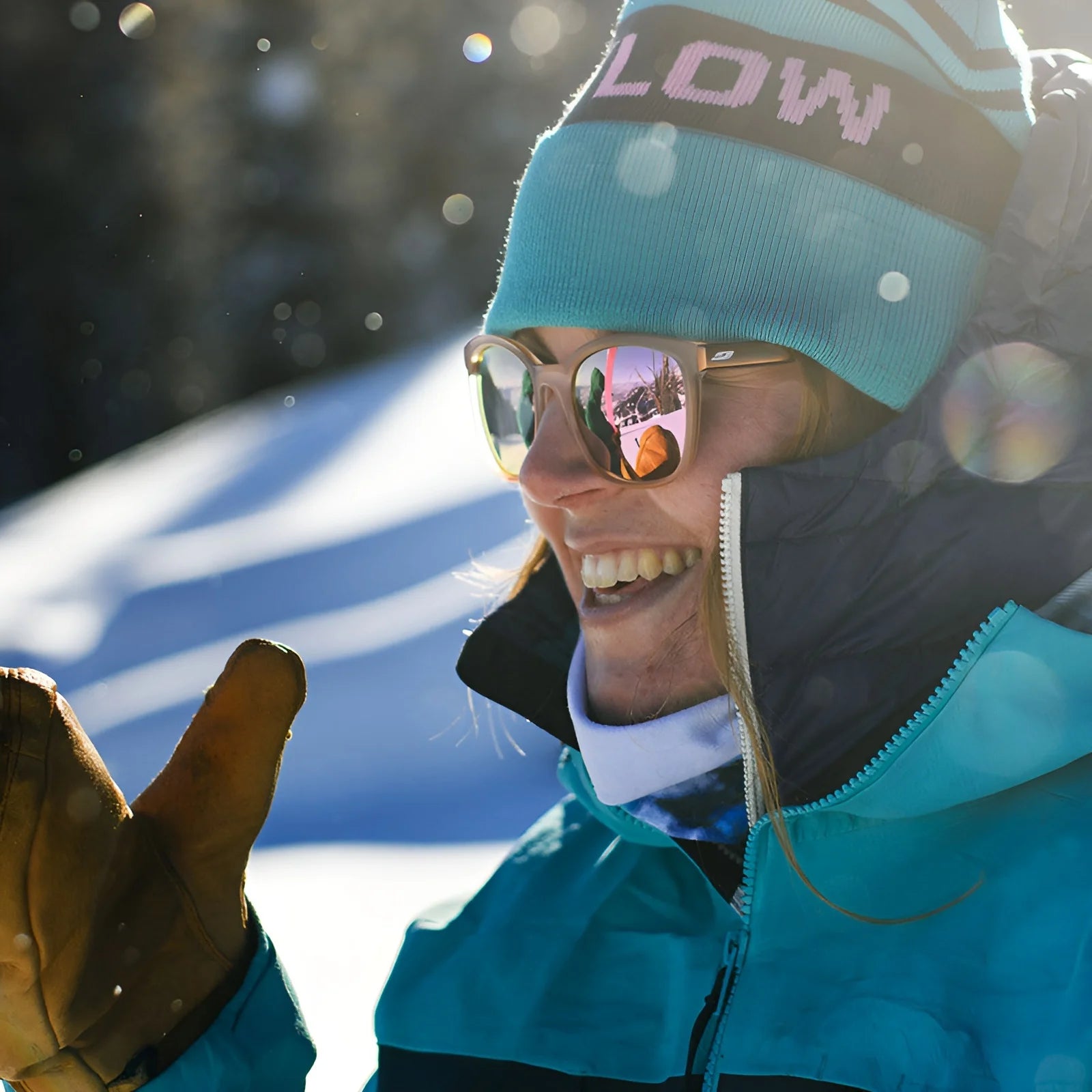Amid falling snowflakes, a person in winter attire smiles wearing Julbo Spark Sunglasses. The lenses reflect snowy landscapes beautifully while Grip Tech Temples ensure comfort and clarity all day.