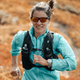 A person jogs through an autumn landscape in a blue jacket and hydration vest, wearing sleek Julbo Split Sunglasses | Size 63 with REACTIV photochromic lenses adapting effortlessly to changing light.