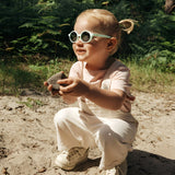 A child wearing Julbo Walk Sunglasses (Size 39) with durable lenses holds a rock while crouching on a sandy forest path.
